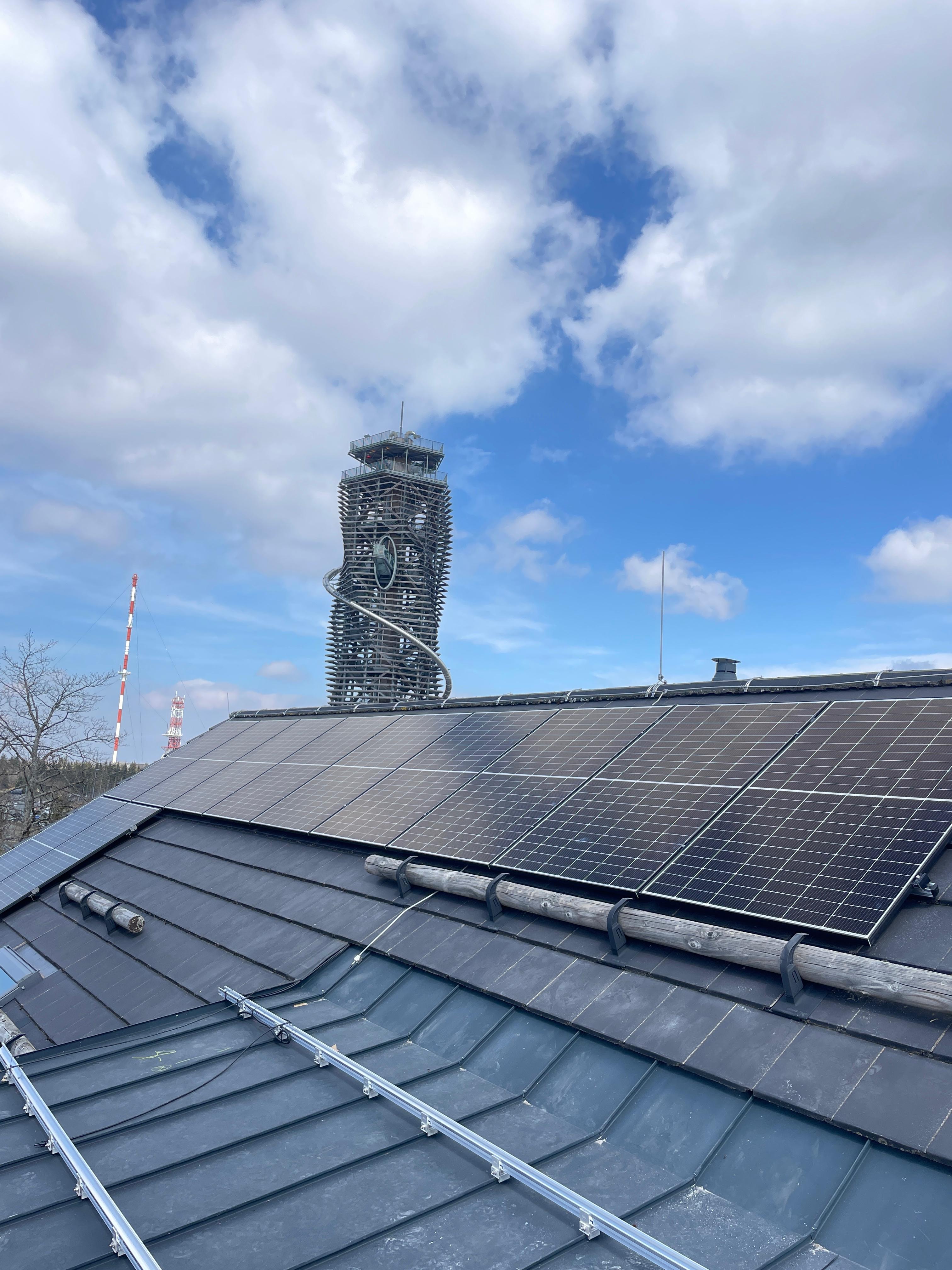Photovoltaikanlage auf Schrägdach mit Aussichtsturm im Hintergrund und blauem Himmel